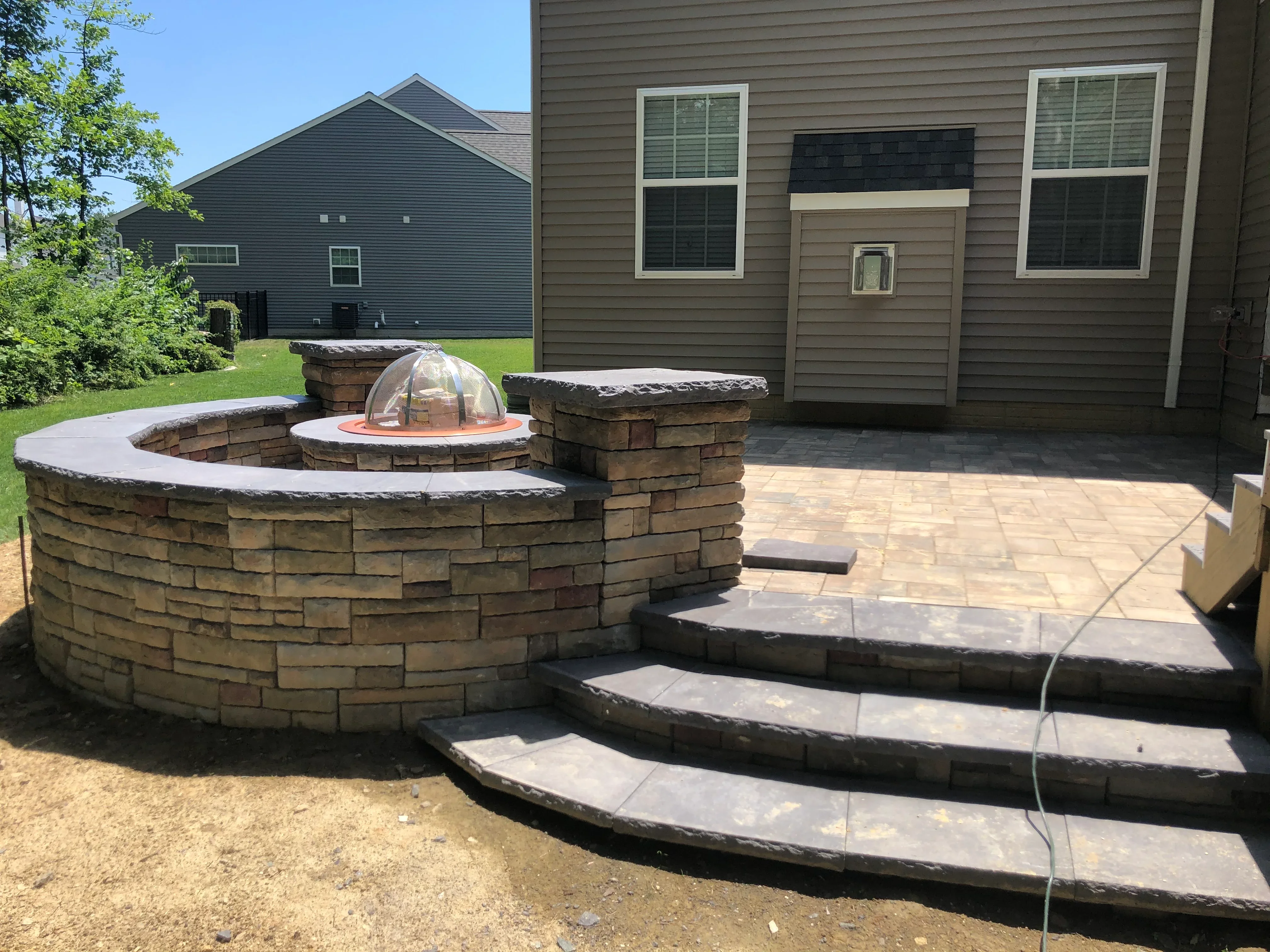 Curved stone fire pit with dome cover and stamped concrete patio with tiered steps