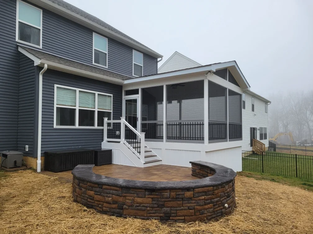Screened porch with white frame and black railings, curved stone fire pit with seating area