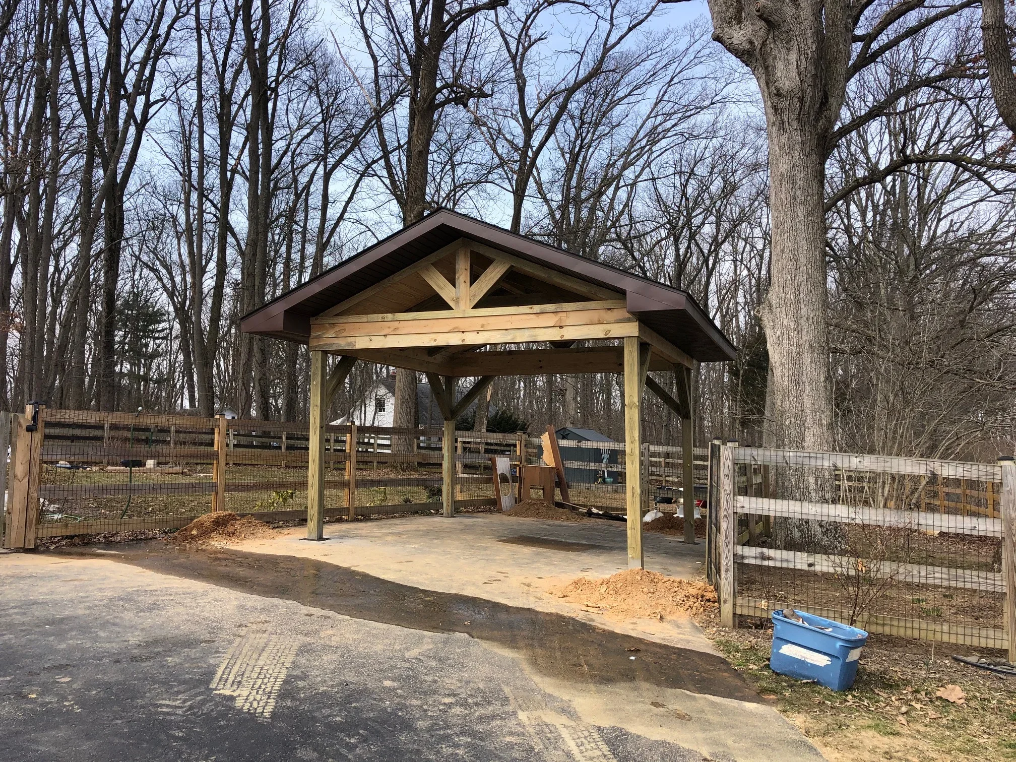 Timber frame pavilion with gable roof, exposed beams, and metal roofing in wooded setting