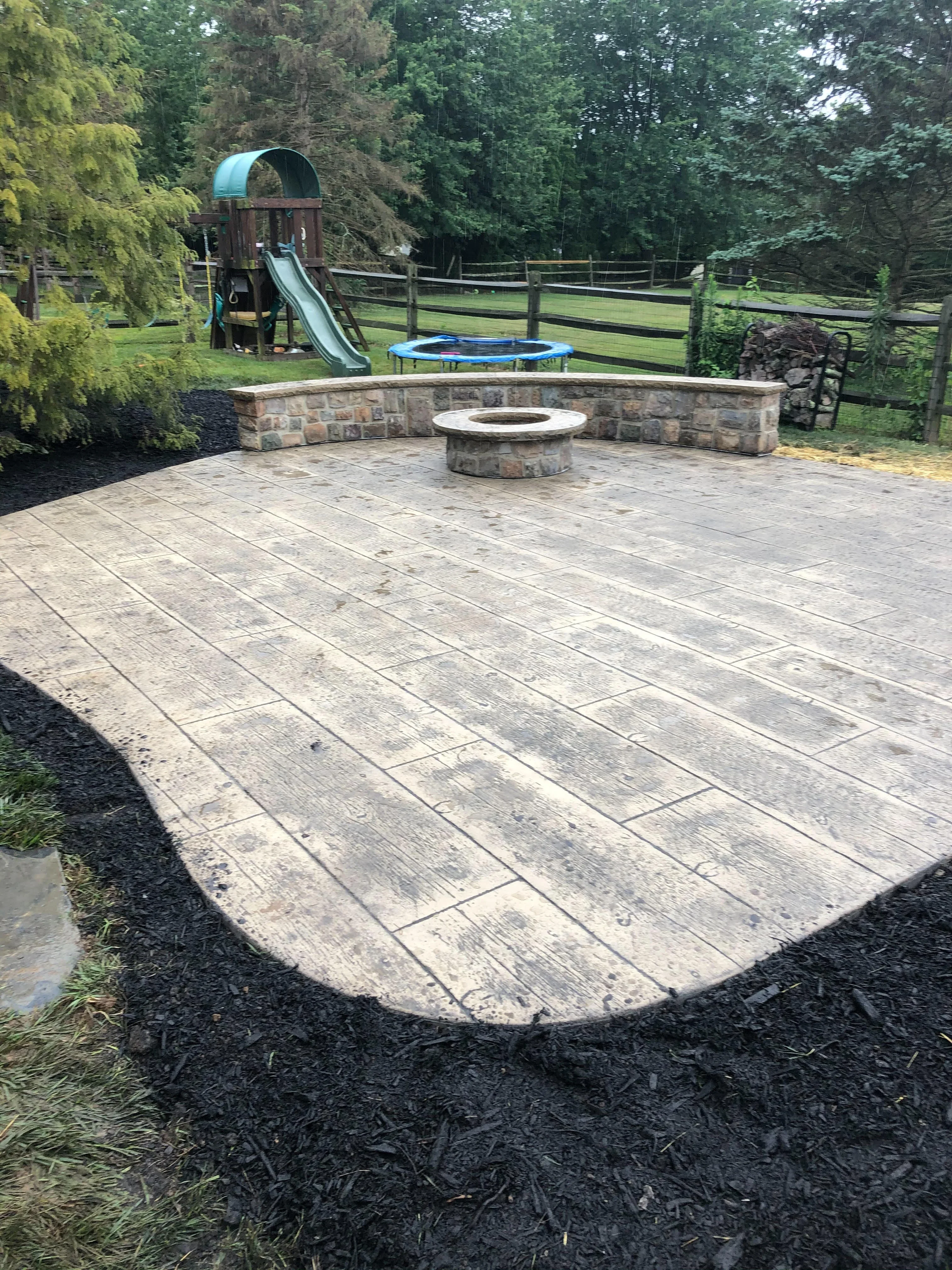 Stamped concrete patio with wood-grain pattern, stone seating wall, and circular fire pit surround