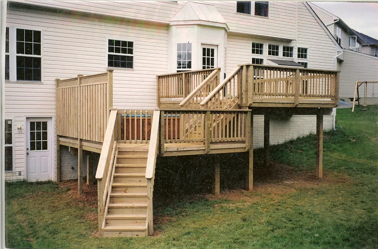 Multi-level pressure-treated wood deck with stairs, railings, and under-deck storage attached to white house