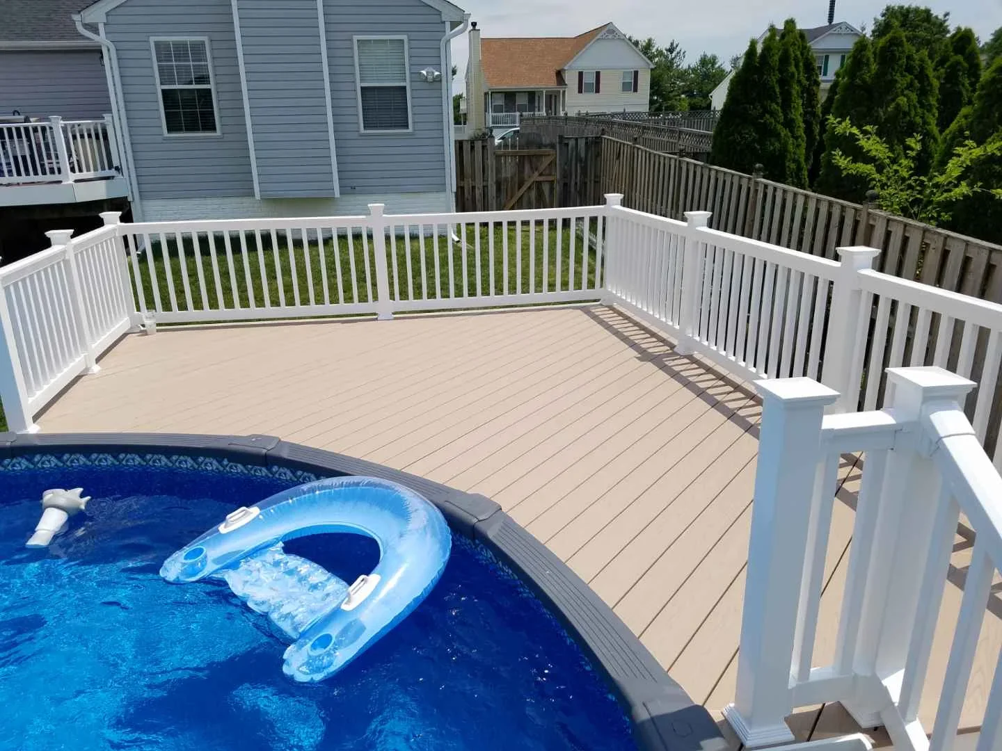 Tan composite deck with white vinyl railing surrounding in-ground pool