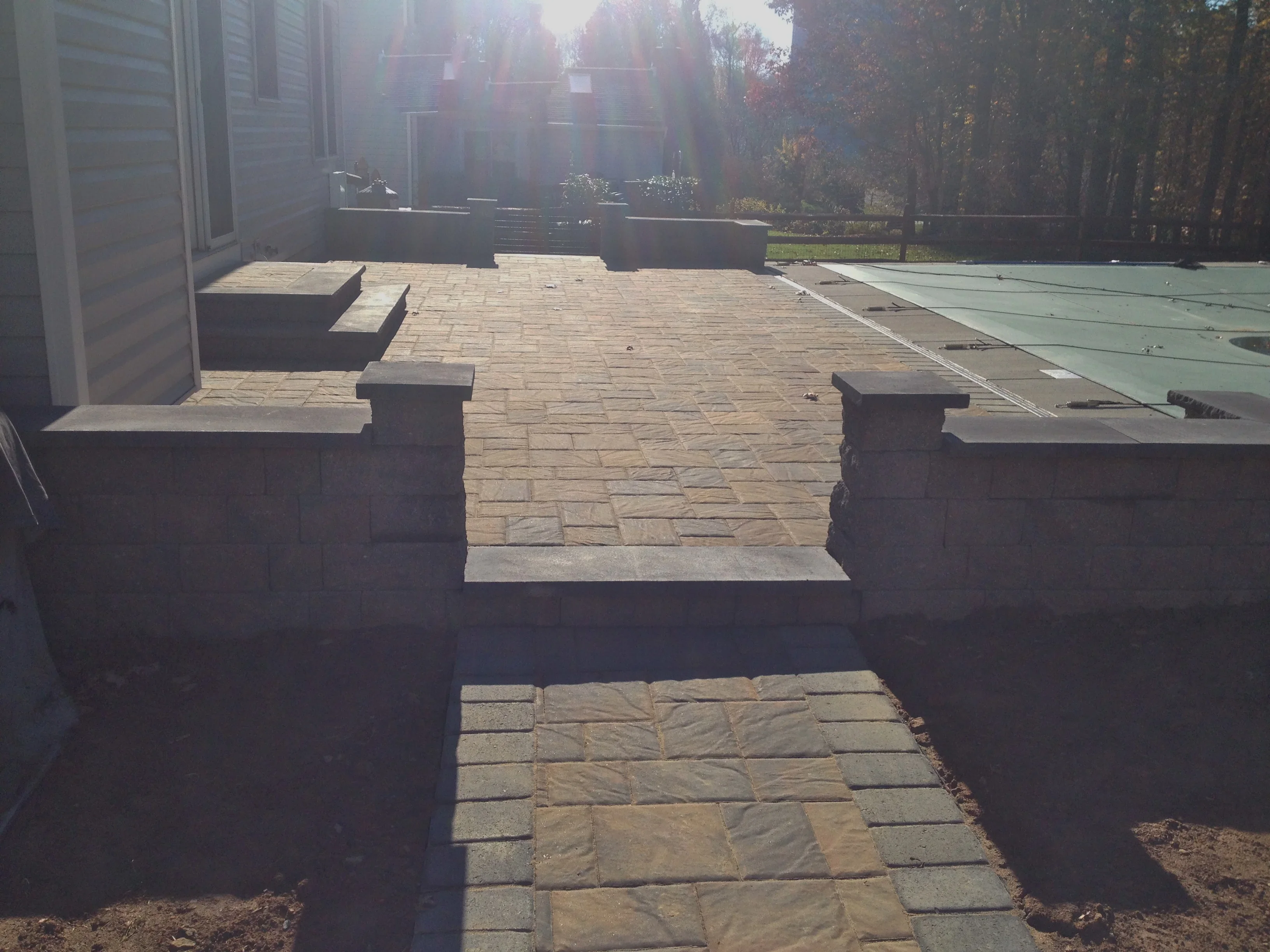 Tan paver patio with concrete retaining walls and cap stones, wooded backdrop