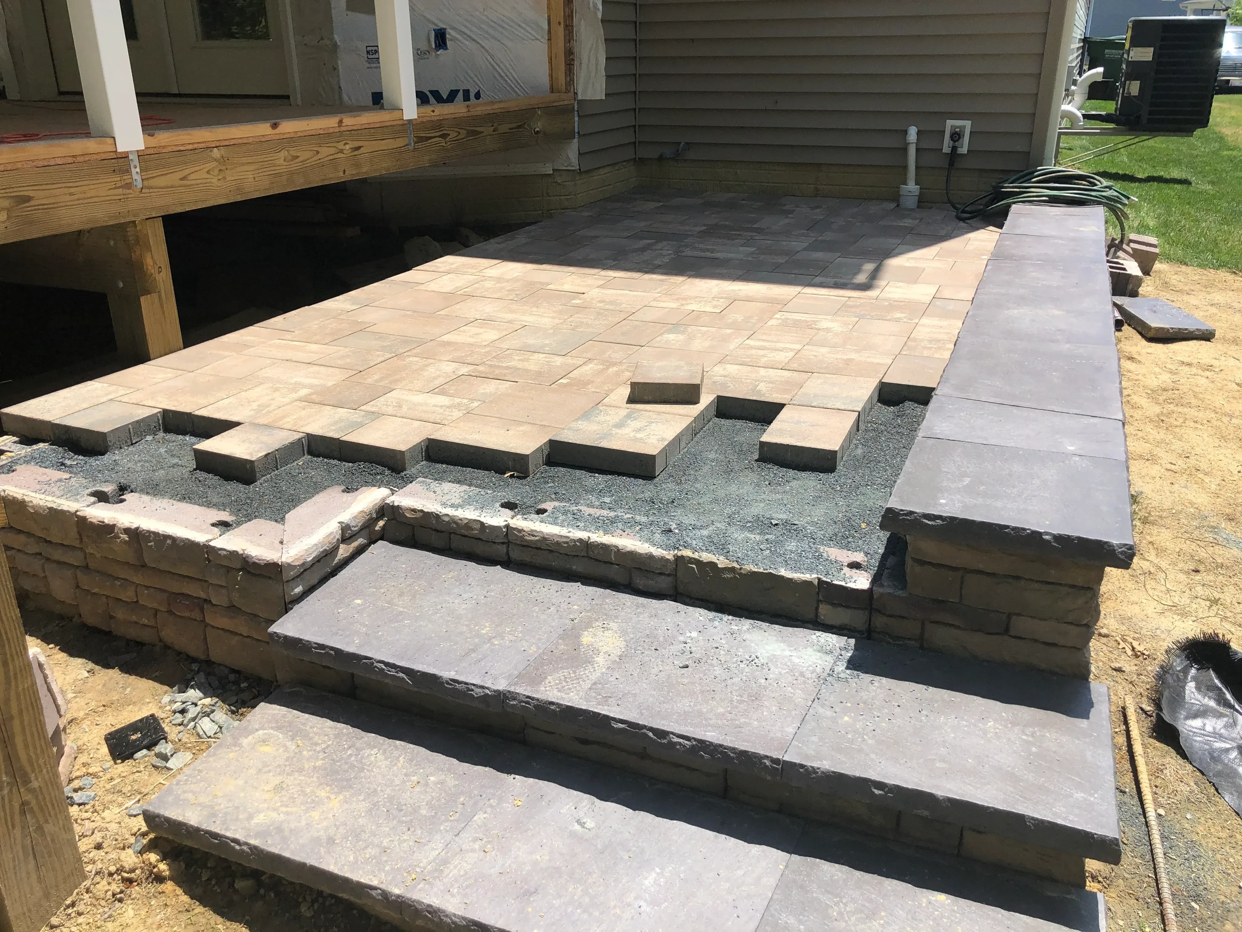 A newly installed ground-level patio in a Harford County, Maryland backyard, showing a clean hardscape surface with defined edges and a clear slope away from the home's foundation. The surrounding yard reflects a typical Maryland residential property with mature trees and an attached home.